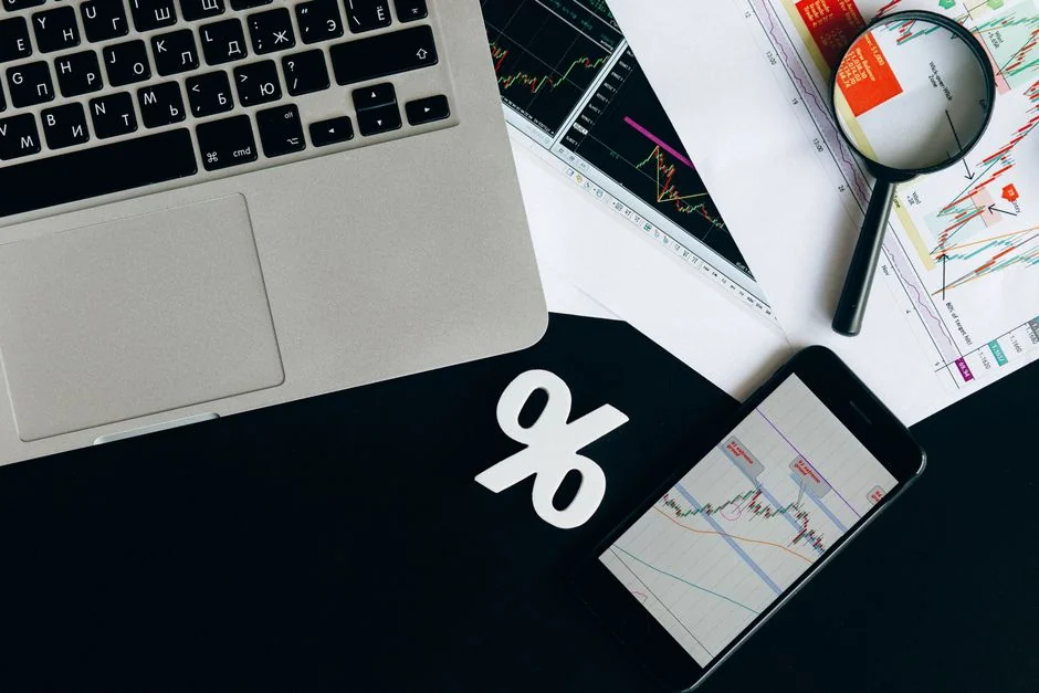 Person analyzes stock data with a smartphone and laptop, indoors.