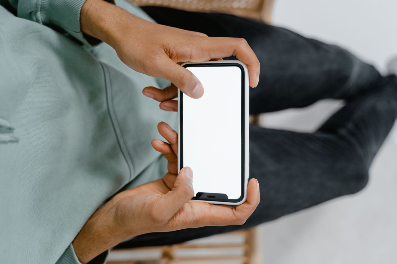 Vue rapprochée de mains tenant un smartphone à l’écran vierge, idéale pour des maquettes d’affichage numérique.